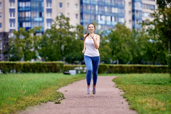 Jonge vrouw joggen in het park in de buurt van meerdere verdiepingen appartementencomplex. — Stockfoto