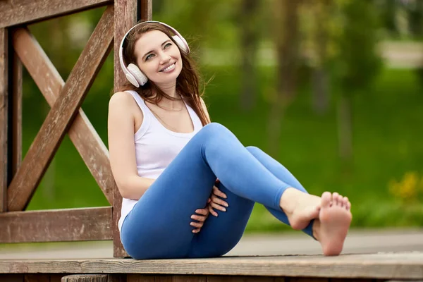 Glückliche schuhlose Frau mit drahtlosen Kopfhörern sitzt draußen. — Stockfoto