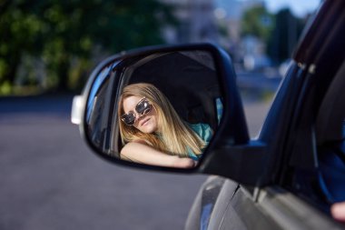 Güneş gözlüklü beyaz kadın dikiz aynasına bakar ve araba kullanır..