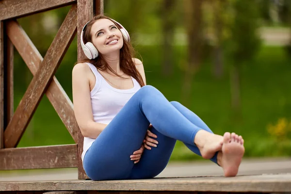 Lächelnde schuhlose Frau mit schnurlosen Kopfhörern hört Musik im Park. — Stockfoto