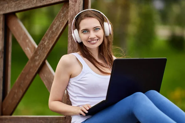 Lächelnde Frau mit Kopfhörer macht Fernarbeit mit Laptop im Freien. — Stockfoto