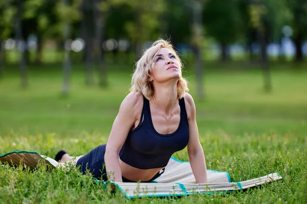 Beyaz kadın, parkta paspasın üzerinde yoga asanas yapıyor.. — Stok fotoğraf