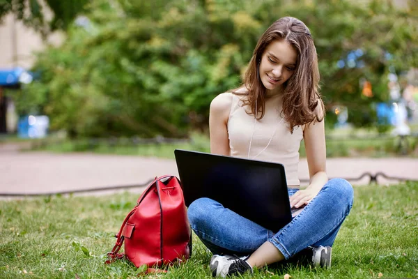 Junge Frau sitzt mit Laptop im Park beim Online-Lernen. — Stockfoto