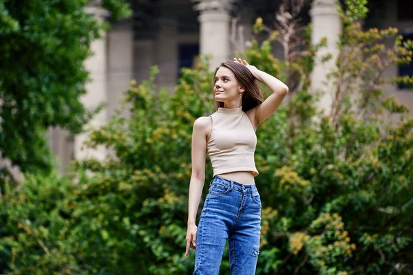 Slim happy female student in jeans stands outdoors. — Stock Photo, Image