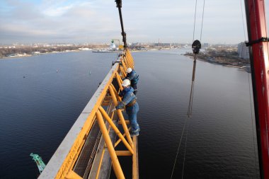 installers working jib fixed to the mast of tower crane. clipart
