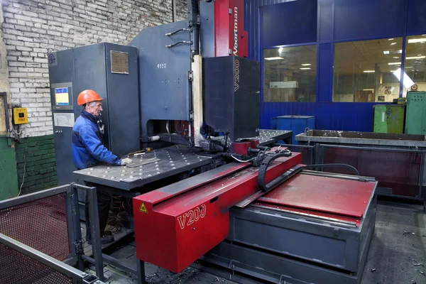 Arbeiter verfolgt die Arbeit der Maschine zum Bohren von Stahlplatten. — Stockfoto