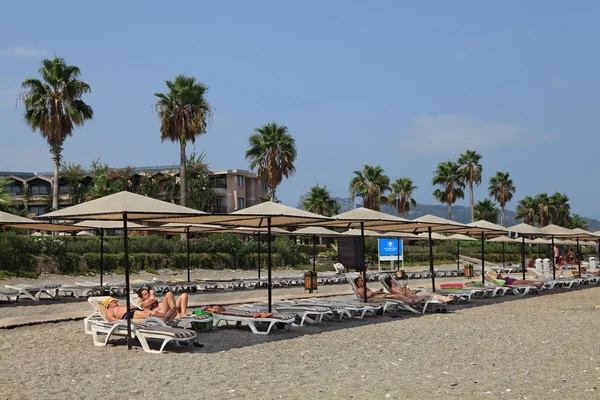 Tourists lying on the loungers private beach in Mediterranean resort. — Stock Photo, Image