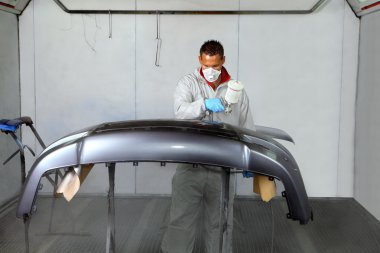 Painters use spray guns to apply paint to a bumper. clipart