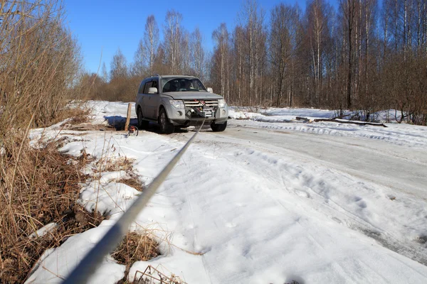 Icy road in forest, cable runs from winch stuck vehicle.