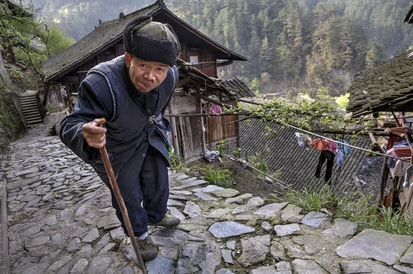 Aged Asian walks along stone road, laying on his stick. — Stock Photo, Image