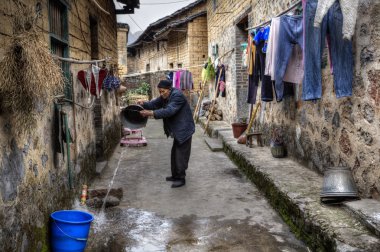 Asyalı yaşlı köylü dar sokak kova su dökülen.