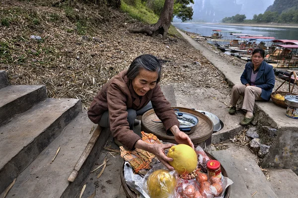 Sonriente mujer china comercia fruta en los pasos que conducen al muelle . — Foto de Stock