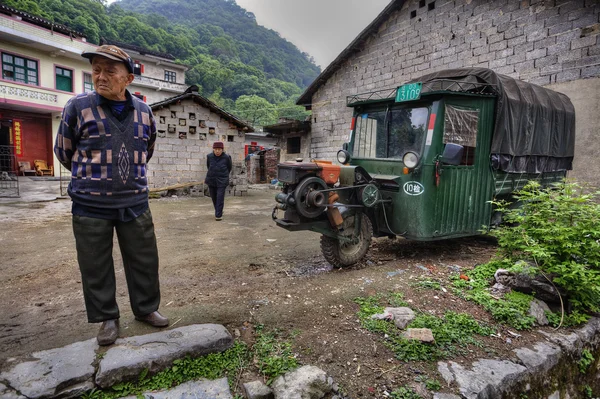 Camponeses chineses na rua da aldeia, ao lado de três rodas verdes — Fotografia de Stock