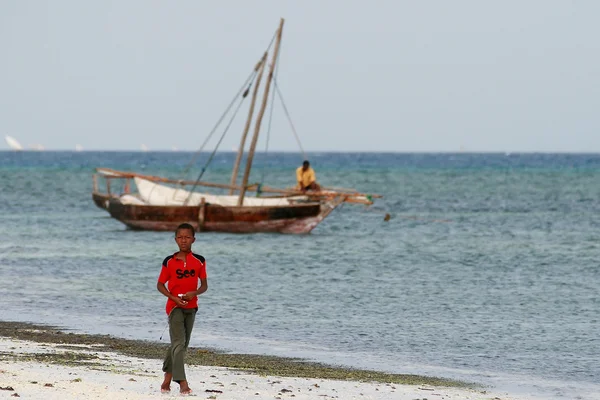 Adolescente niño camina en la costa Océano Índico, cerca de barco de pesca . — Foto de Stock