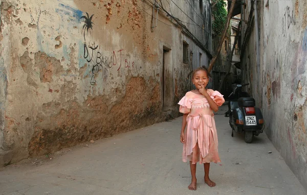 African girl smiling, standing in a courtyard dilapidated stone houses.
