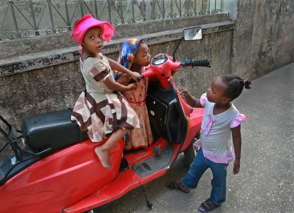 Kolme pientä tyttöä leikkii lähellä afrikkalaista pysäköityä punaista skootteria . — kuvapankkivalokuva