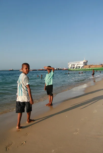 Dos chicos africanos, caminando a lo largo de la playa de arena de la costa, Zanzíbar, Tanzania . — Foto de Stock