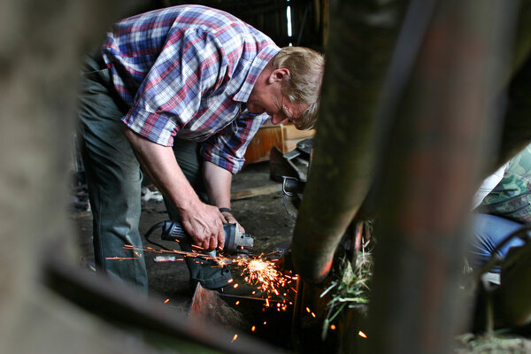 Farmer repairing lawn mower in wooden barn, sharpens knives.