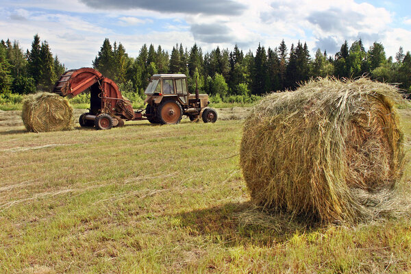 Farmer tractor with baler spitting out round rolls of hay.