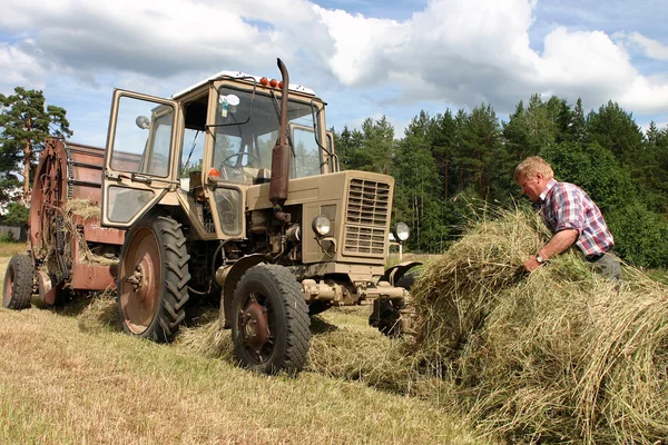 Żniwa czas siana, rosyjski rolnik traktor sterownik pracuje w hayfield — Zdjęcie stockowe