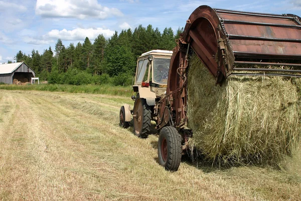 Farm traktor húzza körbálázó miközben széna készítés. — Stock Fotó