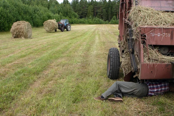 Bestuurder van de trekker reparatie rondebalenpers in het veld. — Stockfoto