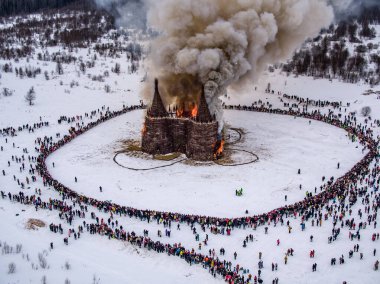 İnsanlar 13 Mart 2021 'de Rusya' daki Nikola-Lenivets sanat parkında düzenlenen Maslenitsa (Shrovetide) festivalinde şato şeklinde ahşap bir yapının yanmasını izliyor.