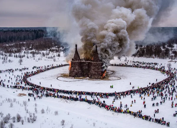 İnsanlar 13 Mart 2021 'de Rusya' daki Nikola-Lenivets sanat parkında düzenlenen Maslenitsa (Shrovetide) festivalinde şato şeklinde ahşap bir yapının yanmasını izliyor.