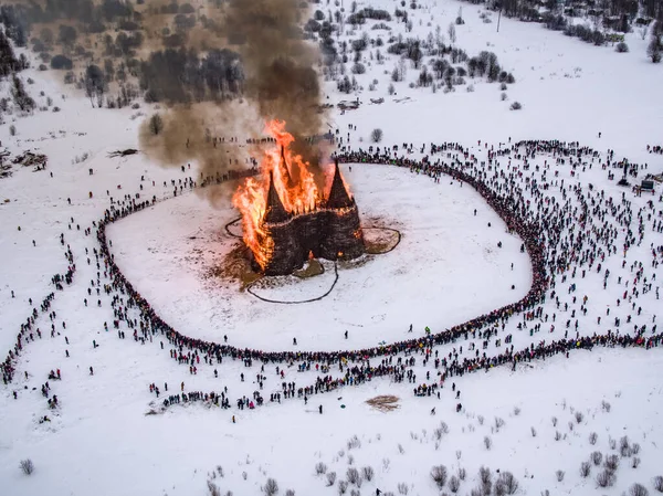 İnsanlar 13 Mart 2021 'de Rusya' daki Nikola-Lenivets sanat parkında düzenlenen Maslenitsa (Shrovetide) festivalinde şato şeklinde ahşap bir yapının yanmasını izliyor.