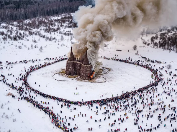 İnsanlar 13 Mart 2021 'de Rusya' daki Nikola-Lenivets sanat parkında düzenlenen Maslenitsa (Shrovetide) festivalinde şato şeklinde ahşap bir yapının yanmasını izliyor.