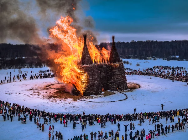 İnsanlar 13 Mart 2021 'de Rusya' daki Nikola-Lenivets sanat parkında düzenlenen Maslenitsa (Shrovetide) festivalinde şato şeklinde ahşap bir yapının yanmasını izliyor.