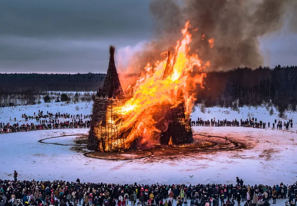 İnsanlar 13 Mart 2021 'de Rusya' daki Nikola-Lenivets sanat parkında düzenlenen Maslenitsa (Shrovetide) festivalinde şato şeklinde ahşap bir yapının yanmasını izliyor.