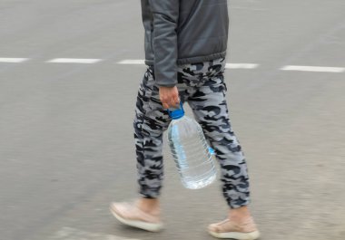 Elinde büyük bir şişe su olan bir adam caddeyi geçiyor. 