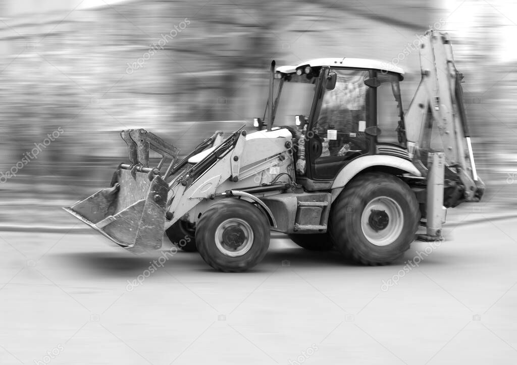 Blurred silhouette of a front loader excavator moving between houses