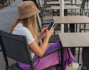 Cep telefonu olan bir kız sokak kafesindeki bir masada oturuyor. 