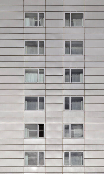 Close up of a grey modern concrete highrise building with geometrical metallic cladding and repeating windows