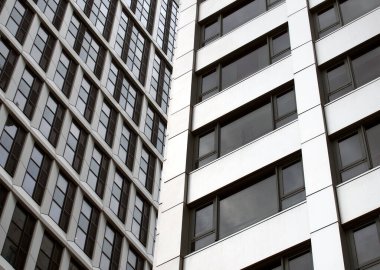 Beyaz kaplamalı ve koyu renkli pencereli yüksek güllü modern apartmanların detaylarını kapat.