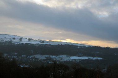 Calderdale Batı Yorkshire 'da karla kaplı, bulutlu bir kış gökyüzünde parlayan turuncu günbatımının panoramik görüntüsü