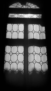 Güneş ışığının kapalı perdelerden parlayan tek renkli atmosferik görüntüsü eski bir pencerenin silüetinde.