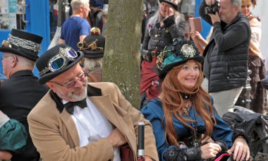 Hebden Köprüsü, Batı Yorkshire, Birleşik Krallık - 01 Ağustos 2021: kostümlü insanlar yıllık Hebden Köprüsü Steampunk hafta sonu bankta oturdu