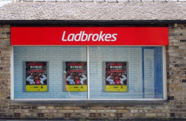 brighouse, west yorkshire, united kingdom - 21 july 2021: sign and front window display of a ladbrokes betting shop in brighouse west yorkshire clipart