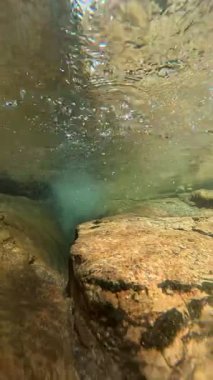 Dalgalanmanın altında, tatlı su akıntısı ve taşlı yatağının huzurlu su altı perspektifi var..