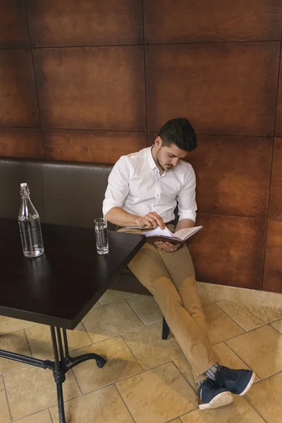 Giovane uomo che legge pianificatore quotidiano mentre è seduto sul divano — Foto Stock