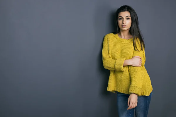 Fille aux cheveux noirs en pull lumineux appuyé sur le mur gris — Photo