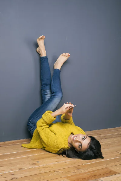 Retrato de hermosa morena sonriente con teléfono acostado boca abajo — Foto de Stock