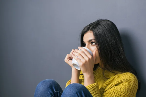 Chica de pelo negro bebiendo de la taza contra de la pared gris — Foto de Stock