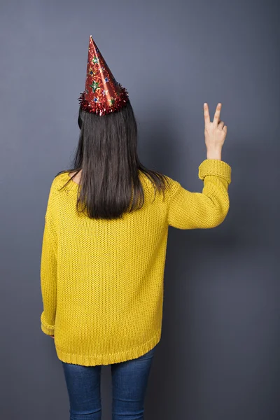 Back view of girl with black hair in festive hat showing peace sign — Stock Photo, Image