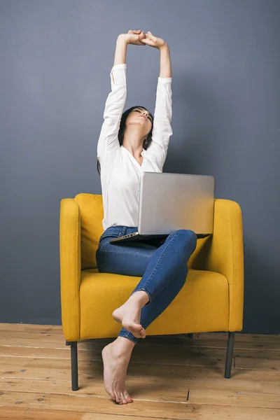 Уставшая девушка с ноутбуком на коленях вытягивает руки — стоковое фото
