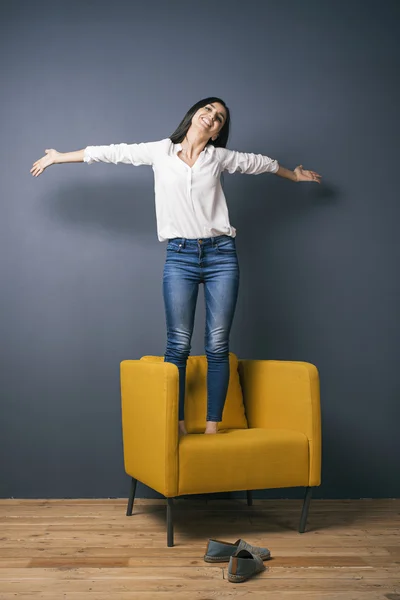 Happy model on yellow chair with widened arms — Stock Photo, Image