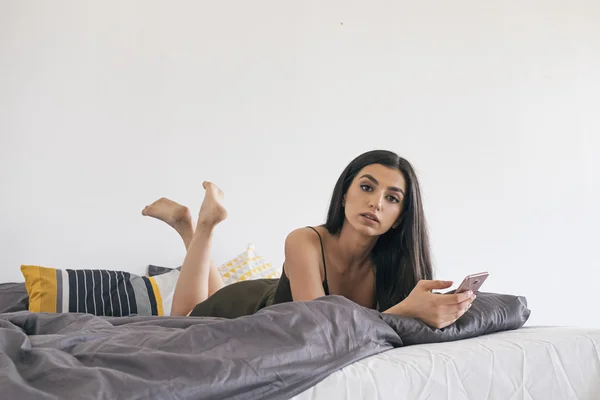 Спокойная красивая девушка смотрит на камеру в постели с камерой — стоковое фото